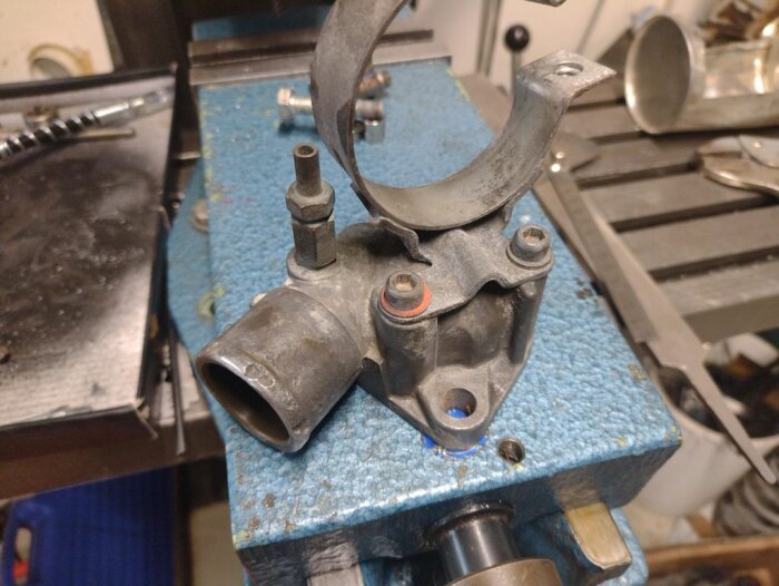 Termostathus satt i ett skruvstäd, med synliga infästningar och röret där termostaten monteras. Verkstadsbakgrund.