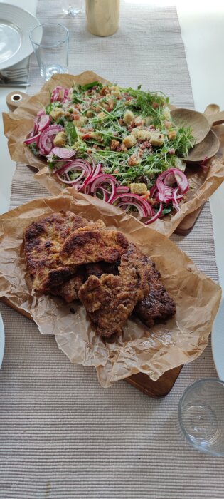 Schnitzel med en unik version av ceasarsallad, inklusive krutonger och skivad rödlök, serverad på bakplåtspapper.