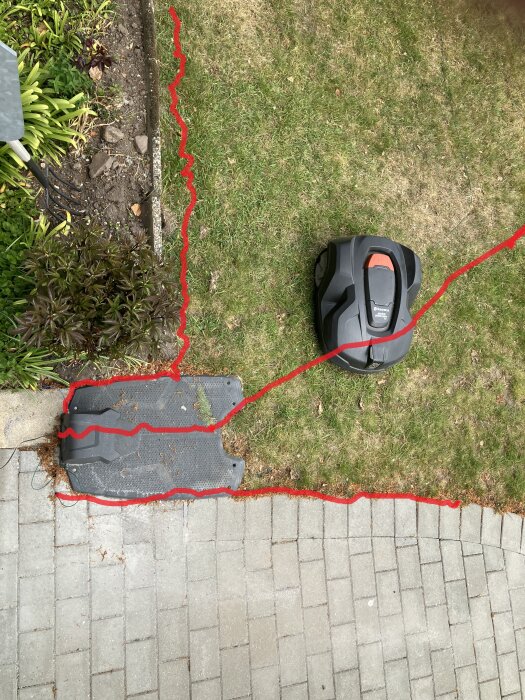 Robotgräsklippare på gräsmatta med röda markeringar av oordnad kabeldragning längs gräset och stenplattor.