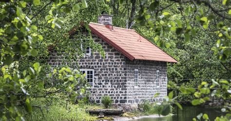 Litet stenhus med rött tak omgiven av grönska, liknande en lada byggd av sintersten.