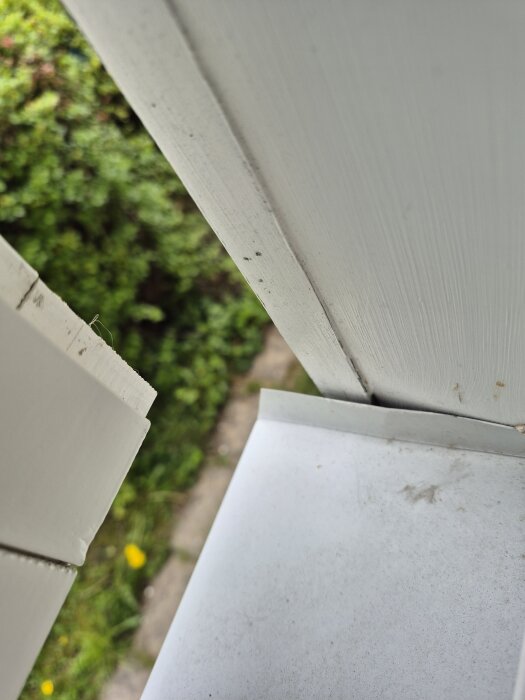 Fönsterbleck på villa med synlig glipa och fråga om tätning med plåtspik och utefog. Buskar i bakgrunden.