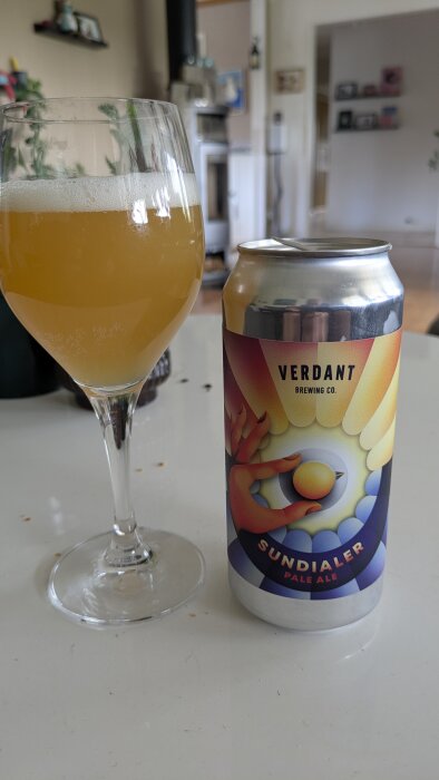 Ett glas med ljus öl bredvid en burk Verdant Brewing Co. Sundialer Pale Ale på ett bord i ett vardagsrum.