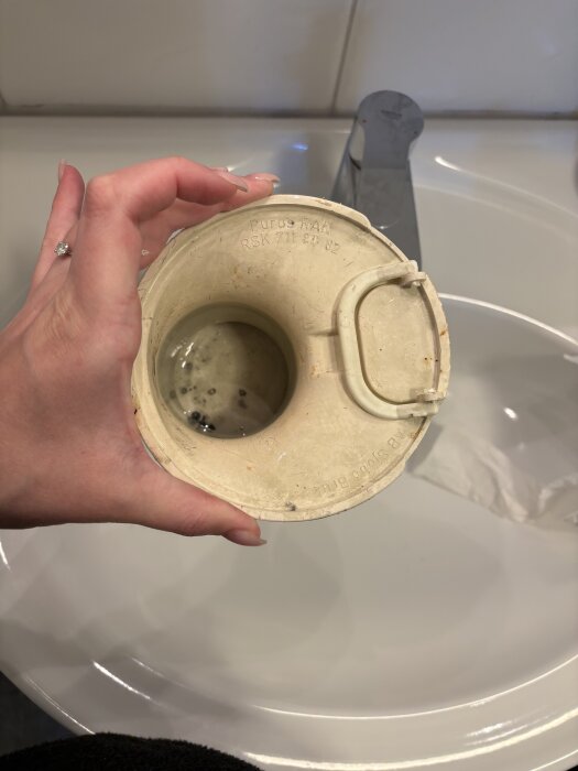 En hand håller i ett brunnslock ovanför ett handfat, visas uppifrån.