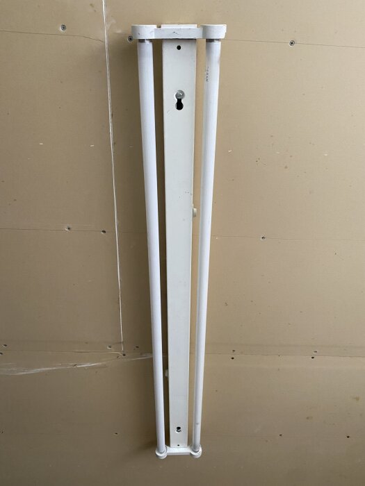 Gammal lysrörsarmatur monterad på vägg med två lysrör, svår att öppna, tillverkad i England, utan synlig märkning.