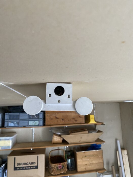 Vit lysrörsarmatur monterad i taket, omgiven av hyllor med förvaringslådor och diverse föremål.