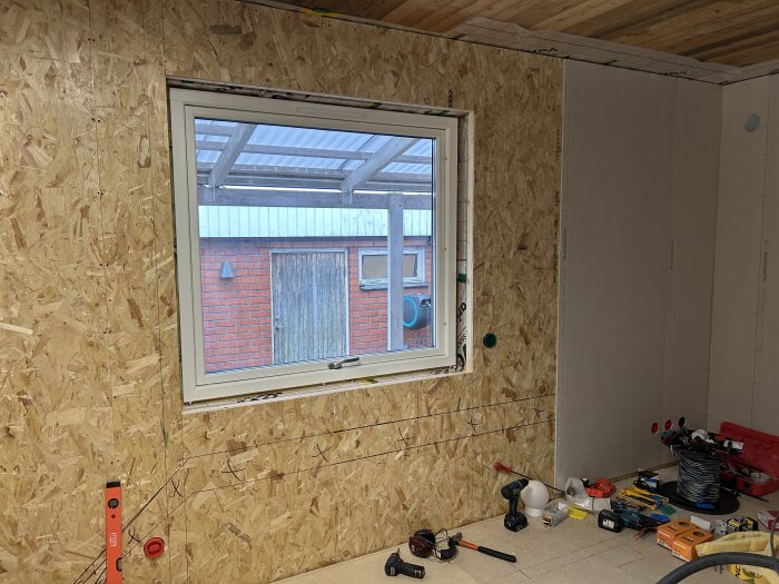 Nytt fönster installerat i rum med träväggar, verktyg och material utspridda på golvet.