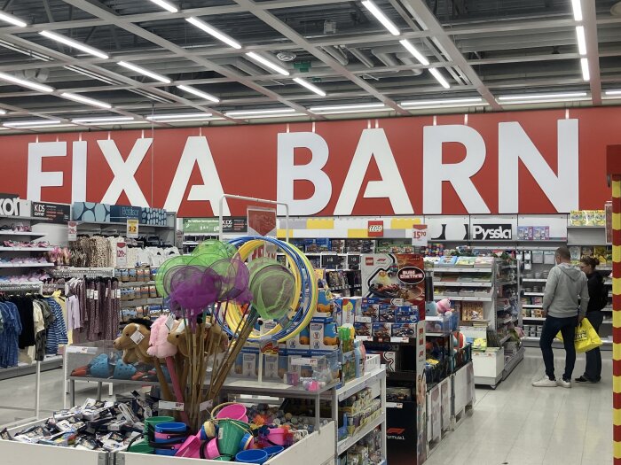 Hylla i Ica Maxi med texten "Fixa Barn" ovanför, med leksaker och andra barnartiklar omkring.