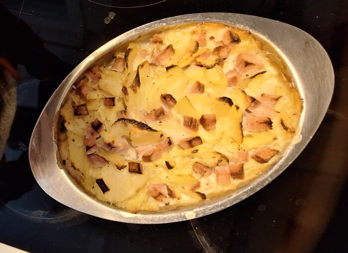 Potatisgratäng med kassler i ugnsform, delvis gratinerad på toppen.