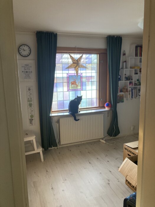 Blyinfattad glasskiva med motiv av kronhjort i ett fönster, en svart katt sitter på fönsterbrädan.