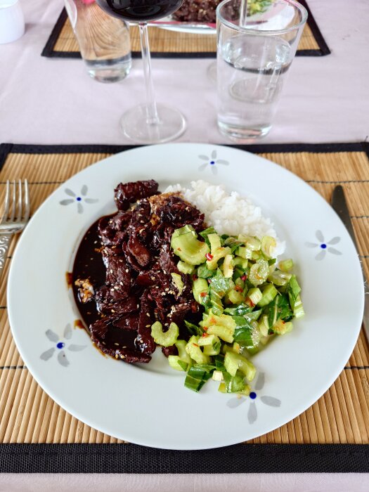 Lövbiff teriyaki med sås, ris och pak choi sallad på en vit tallrik, serverat med ett glas rött vin och ett glas vatten.