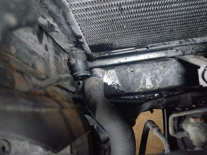 Rostig bilkylare och kylarslang med spilld kylvätska och fuktigt fläckat område runtom.