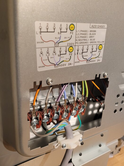 Elektrisk anslutning med olika färgade ledningar kopplade till en terminalblock på en apparat, med kopplingsschema ovanför.