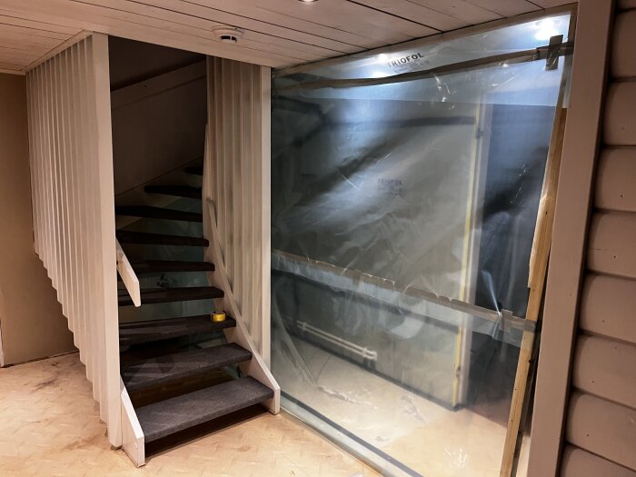 Inplastat utrymme för renovering med en trappa bredvid, del av ett bygge för att byta rör och minimera dammspridning.