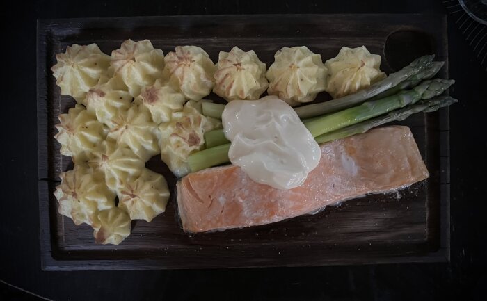 Laxplanka med pressad potatis, sparris och hollandaisesås på träplanka.