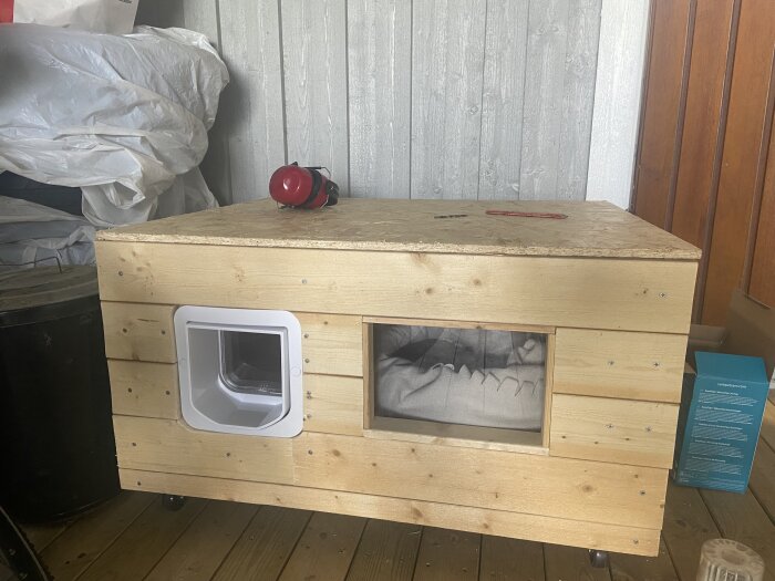 Isolerat kattkrypin med OSB-skiva som tak och kattlucka, byggt för att hålla katten ute på nätterna; står på en träveranda.