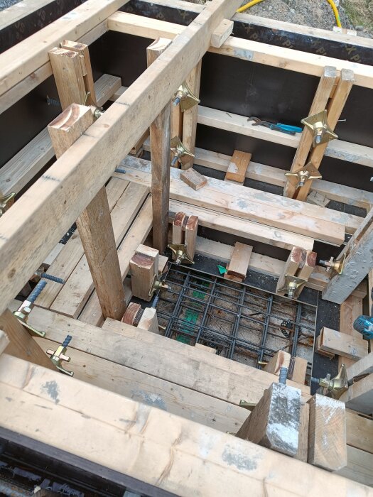 Form för gjutning med träbalkar och gjutluckor, armeringsjärn synliga i botten. Verktyg är placerade intill.