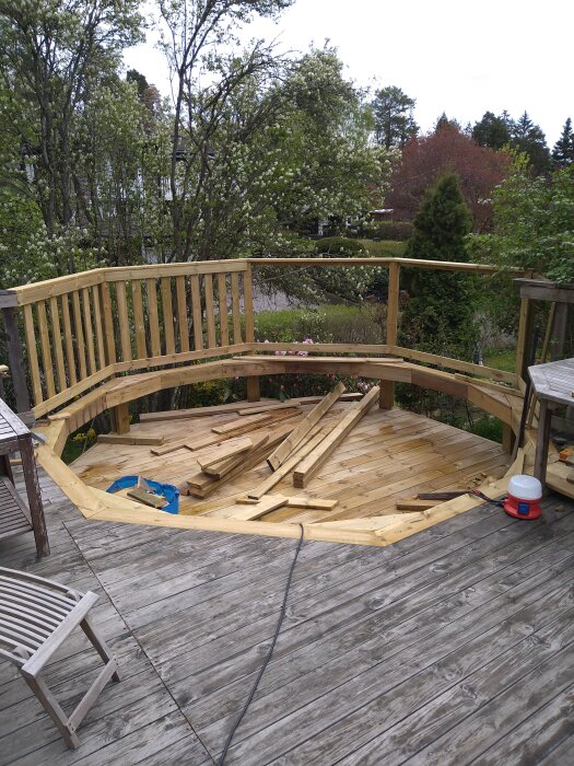 Träaltan under konstruktion med höga träd i bakgrunden och några verktyg och träplankor på golvet.