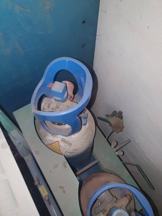 Gasflaska med blå inbyggd regulator, märkt 584742, i ett förvaringsutrymme.