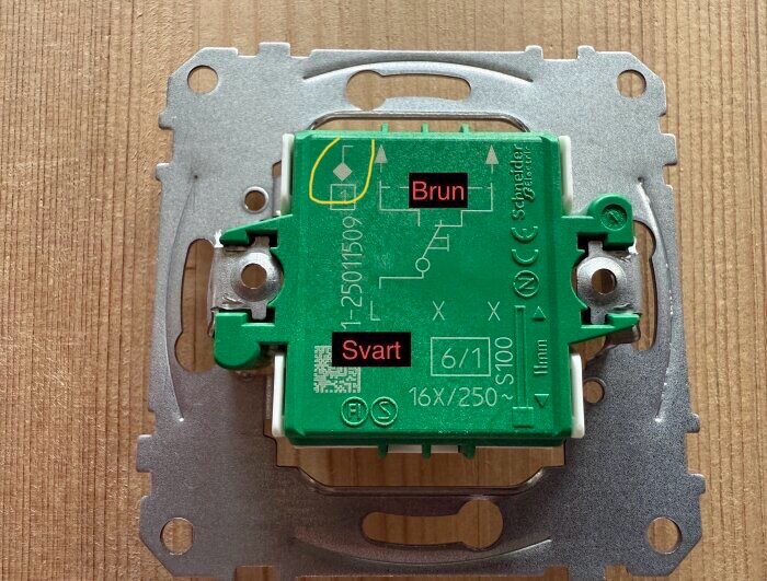 Elektrisk brytare med brun och svart markerade anslutningar på en grön bakgrund, monterad på en träribbad yta.