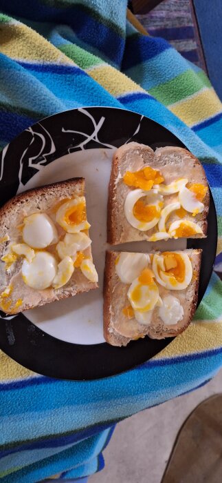 Kaviarmackor med svårskalade ägg på en svart tallrik, placerade på en randig filt.