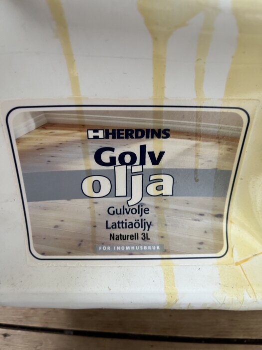 Behållare av Herdins golvolja, naturlig, 3 liter, med etikett som visar ett oljat trägolv och oljefläckar på behållarens yta.