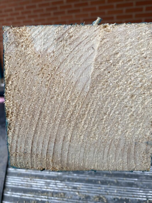 Närbild av ändträ på en bit 100x100 mm konstruktionsvirke, med sågspår och grov textur, för byte till 90x90 mm limträ diskuteras.