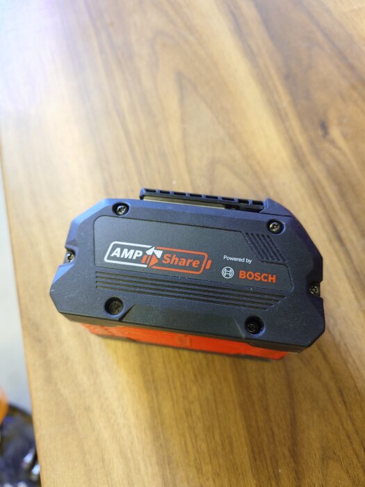 Batteri från AMPShare med Bosch-logotyp på ett träbord.