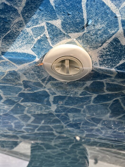 Anslutningen till ett poolutlopp med en fast vinterplugg, omgiven av blå mosaikbelagd yta.