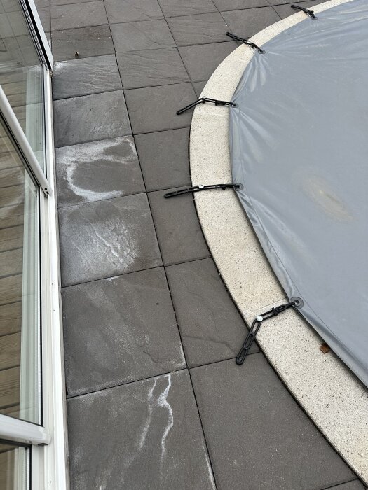 Täckt pool med kant av stenplattor vid glasvägg. Svårt att nå utloppet under stenplattorna.