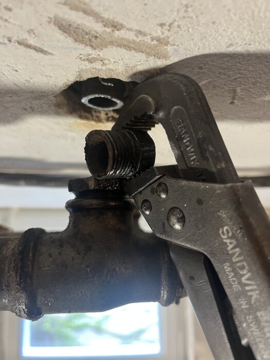 En rörtång används för att lossa en t-kopplings bussning från ett avloppsrör under ett tak.