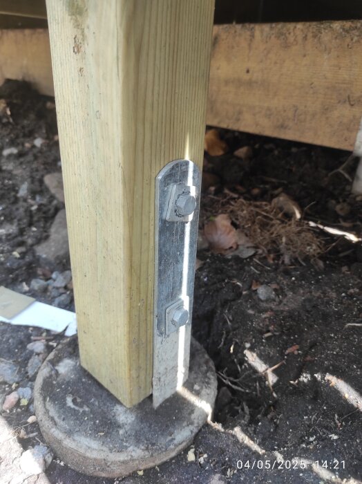 Träregel fäst med metallbeslag och bultar i betongfundament utomhus.