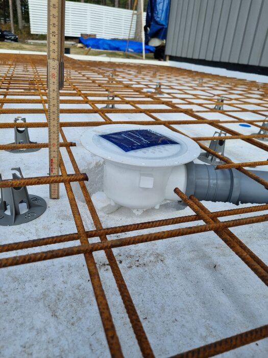 Armeringsnät över cellplast med golvbrunn och linjal som mäter höjden, nätet vilar på distanser. Brunnens sänkning återstår 15 mm.