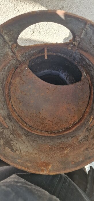 Rostig del av gammal järnkamin där den skadade anslutningen till rökkanalen syns, i behov av reparation eller utbyte.