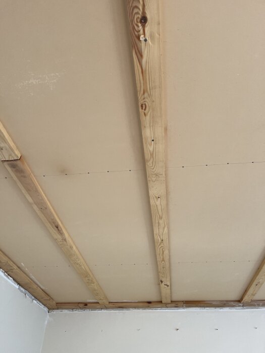 Masonitplattor i innertak med synliga träbjälkar, delvis demonterat i vardagsrum, i ett radhus byggt 1963.