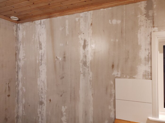 Vägg efter borttagning av tapet och applicering av Zinsser Gardz, med ojämn yta och synliga märkningar, innan spackling och slipning.