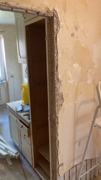 Gamla dörröppningar utan karmar, blottade vägghörn; slitet tapet och inredning syns. Stege och byggmaterial i bakgrunden.