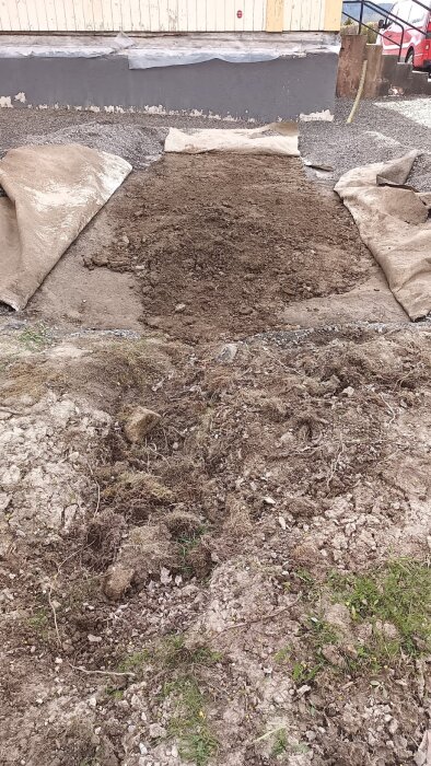 Dike fyllt med jord och grus på en uppfart, omgiven av presenning och ett hus i bakgrunden.