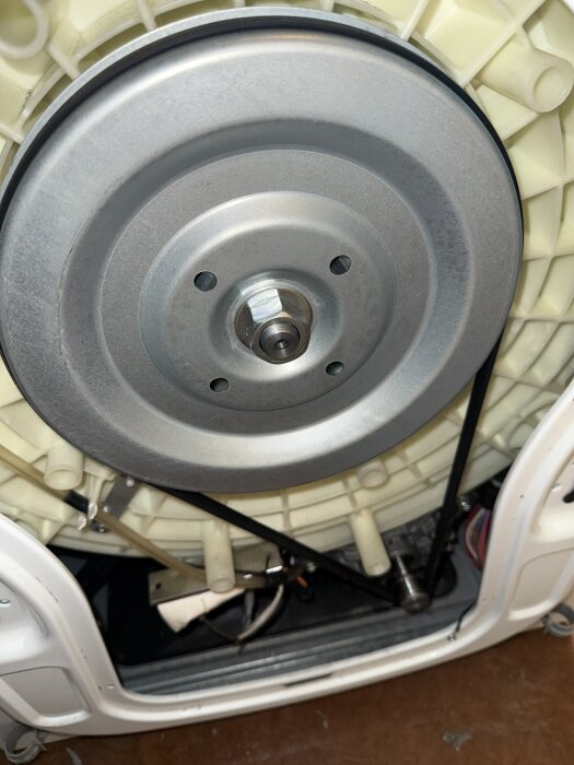 Närbild på tvättmaskinens baksida med ett metallhjul och rem monterad.