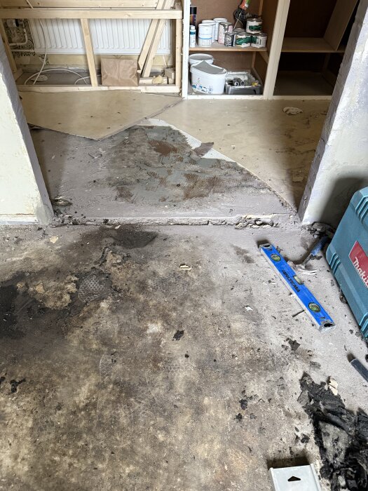 Golvet mellan kök och hall med synligt mellanrum efter borttagen tröskel. Verktyg och byggmaterial syns i bakgrunden.