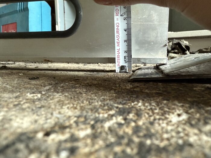 Mätskillnad mellan hall- och köksgolv, visar en nivåskillnad på cirka 7 mm utan tröskel. Röd linjal används för att illustrera höjdskillnaden.