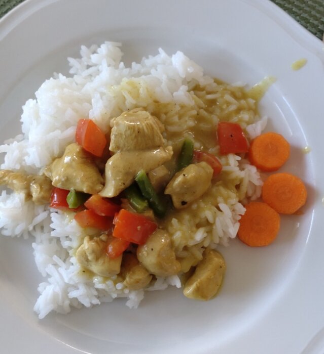 Kyckling- och currygryta med ris, morötter och gröna bönor på en tallrik.