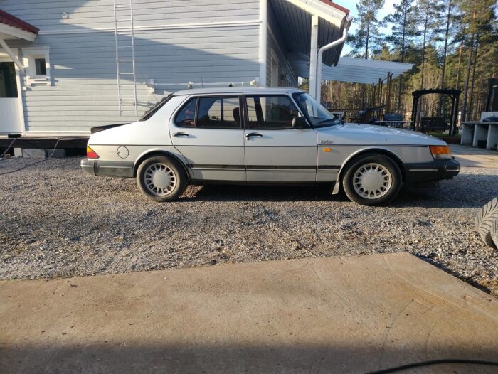 Silverfärgad Saab bil parkerad framför ett vitt hus, utrustad med sänkfjädrar fram och redo för hjulinställning och tvätt inför sommaren.