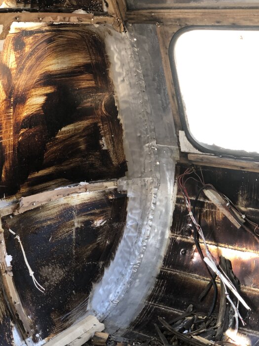 Inre av en husvagn under renovering, med delvis frostade och rengjorda ytor, exponerade träreglar och kablage.