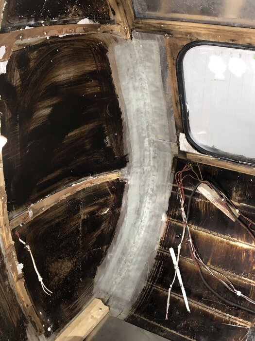 Interiören på en husvagn under renovering med glasfiber och epoxy över hörnet. Gamla kablar och mörka väggar syns inuti vagnen.