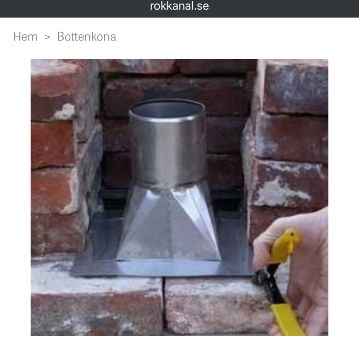 Bottenkona av metall installerad i murad skorsten, hand håller verktyg vid kanten.