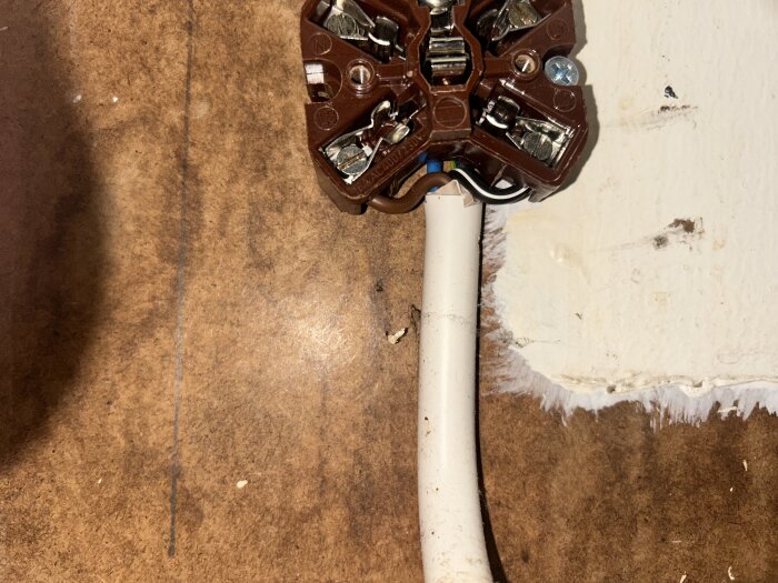 En närbild på en brun perilexkontakt med flera inkopplade kablar, mot trä- och väggunderlag.