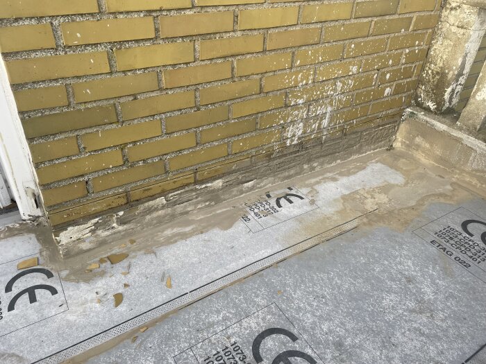 Tätskiktsduk delvis fastsatt på balkonggolv nära tegelvägg, med synliga sprickor och lossnad yta, där installationen diskuterats i forumtråd.