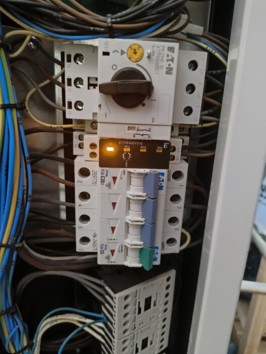 Elpanel med flera brytare och kablage, en av brytarna har en indikatorlampa som lyser. Flera färgkodade kablar är anslutna.