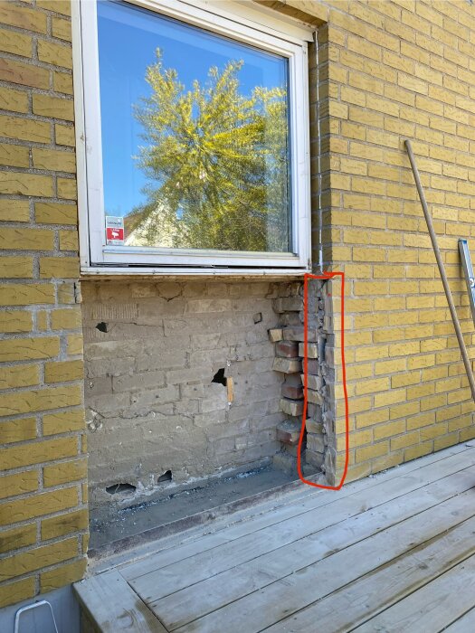 Bilden visar en tegelvägg med ett hål där ett fönster ska ersättas med en dörr. Den rödmarkerade delen är ojämn och utan tegel.
