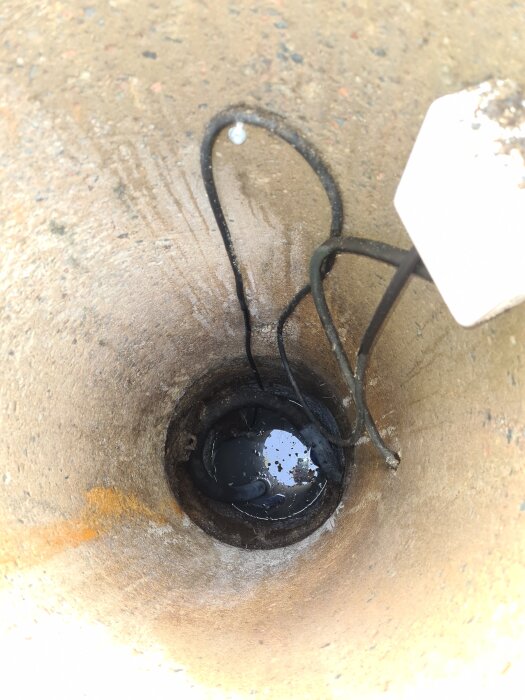 Trekammarbrunn med slitet ingångsrör och kablar, lite stillastående vatten i botten.